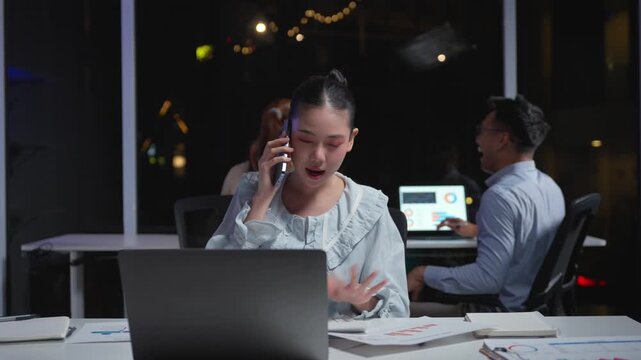 Frustrated young asian businesswoman arguing on a phone call while working late in the office. Busy employee stressed by work overload