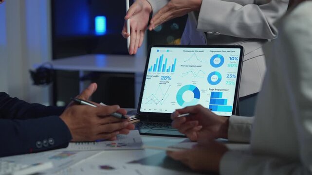 Close up of a collaborative business team meeting late at night, analyzing financial statistics on a tablet and paper documents