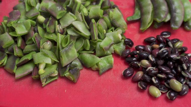 Close-up of hyacinth beans (Lablab purpureus) cut with seeds on red tabletop, organic farm-to-table India