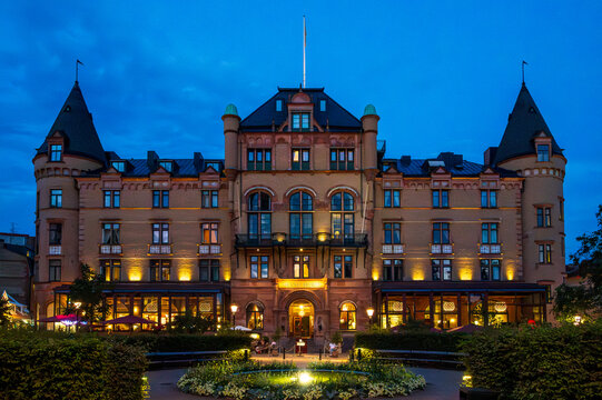 Lund, Sweden - August 8 2020: Illuminated historic grand hotel building with towers at dusk with a fountain in the foreground