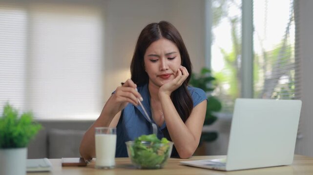 Displeased young woman on a diet reluctantly eating a tasteless salad for lunch. Healthy lifestyle and weight loss nutrition concept