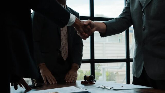 Businessmen and lawyers finalizing a deal by signing documents, shaking hands, and clapping. A successful negotiation in a law office