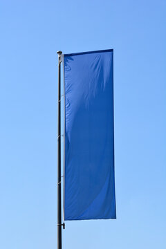 A long rectangular blue banner hangs from a tall metal pole against a clear blue sky background