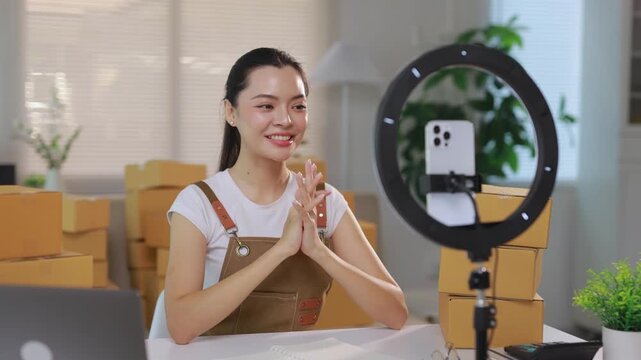 Young Asian woman speaking to her smartphone camera during a live broadcast. Small business owner using social media for e commerce
