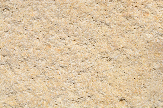 A close up shot of a natural rough yellow limestone wall showing detailed porous texture and uneven surface under bright sunlight