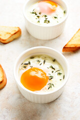 Eggs en cocotte (baked eggs) in ramekins with cream, сheese and greens