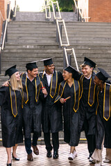 Diverse group of smiling graduates walking together, wearing caps and gowns, holding diplomas after ceremony