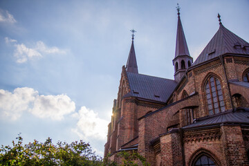 Fototapeta premium Low angle view of a historic red brick gothic church with tall spires and flying buttresses against a blue sky with sun flare in Malmö Sweden