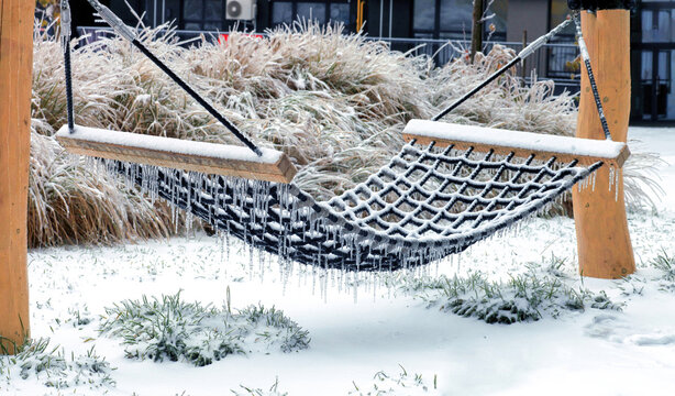 Snow covering and frozen rope hammock with icicles hanging from net in winter garden