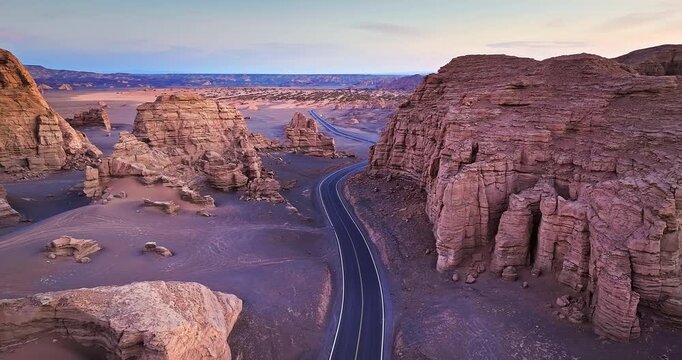 Aerial view of a winding asphalt road through the eroded Yardang landforms and Gobi desert in Xinjiang, China. Empty highway landscape.