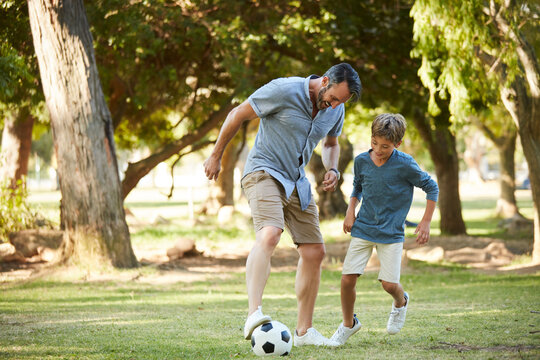 Father, boy and play with football at park for bonding, exercise and fun with teaching, kick and outdoor in summer. People, dad and child with love for soccer, pass or dribble with learning on grass