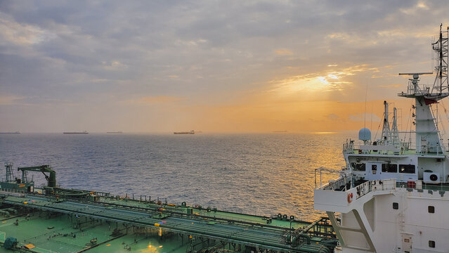 Expansive sunset panorama from large oil tanker deck sailing through calm open sea with dramatic cloud formations and distant cargo ships on horizon