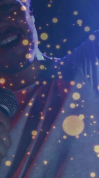 Vertical video: Camera shifting revealing music singer leaning into mic, singing under golden dots