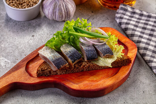 Pickled herring appetizer on rye bread with lettuce, onion, and garlic on a wooden board