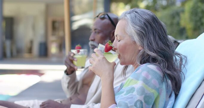 Warm sunlight urging mature couple lounging poolside sipping mint cocktails with strawberry garnish