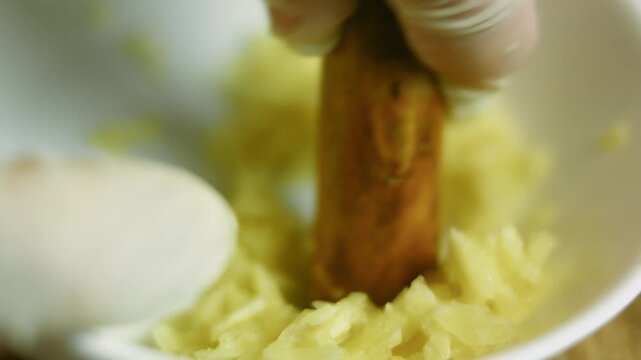 Close up of mashing the garlic cloves in a white bowl