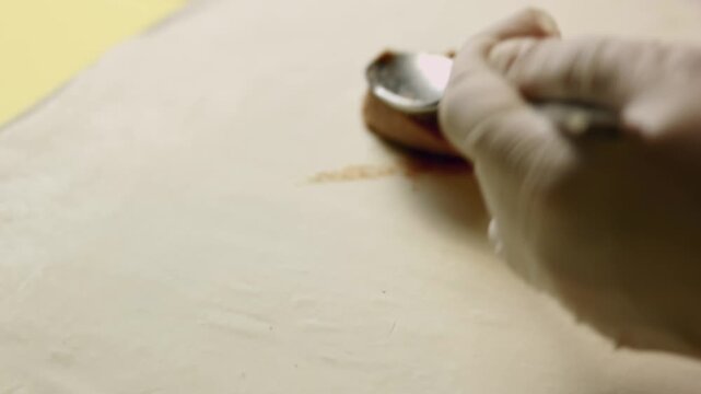 Person is applying meat pate in a thin layer on the sheet of puffy pastry