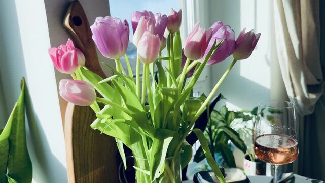 Luxury March 8 breakfast with black caviar, crepes and tulips. Black cat sitting among houseplants on a sunny windowsill. Festive Maslenitsa table setting with white wine and spring flowers.