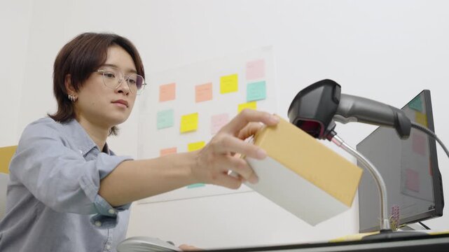 Asian female office worker handle parcel boxes by reading the barcode stickers with a barcode scanner to record the information in the computer.