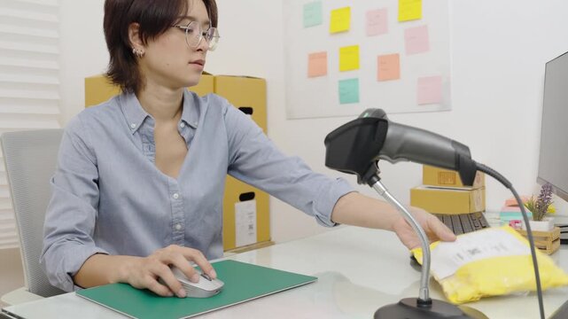 Asian female office worker handle parcel boxes by reading the barcode stickers with a barcode scanner to record the information in the computer.