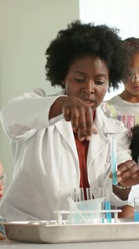 Vertical video: Picking up test tube, lab-coated teacher using dropper at demo table for science