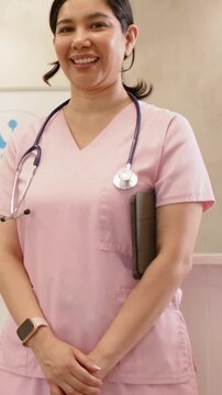 Vertical video: Recording starting nurse in pink scrubs standing at clinic with tablet, stethoscope