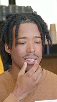 Vertical video: Looking at white card man in tan quilted top reading reacting to content in cafe