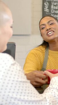 Vertical video: Clapping at POS, customer in blouse taking red mug for pickup from barista in apron