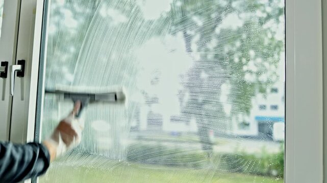 A man washes windows in a house. A cleaning company cleans and washes windows in a house. A professional man washes plastic windows with a solution and a mop.