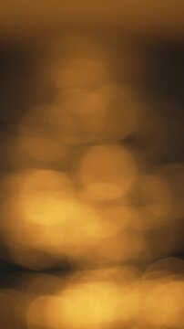 Golden water bokeh, abstract shimmering light reflections create a peaceful and serene backdrop. Vertical video.