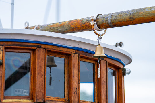 Wooden boat cabin with brass bell hanging from weathered mast.