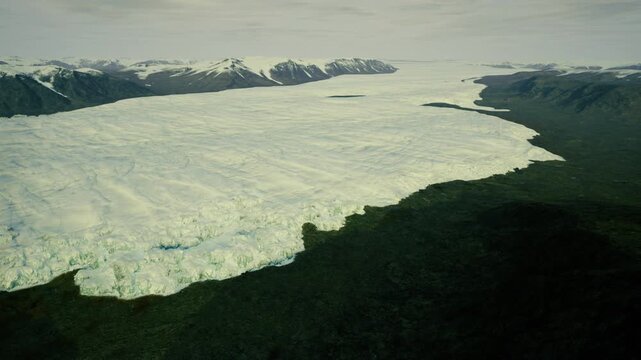 Broad Greenland icecap meeting dark rocky fjord, high contrast lighting and scattered bergs, dramatic scale and raw polar landscape for editorial use.