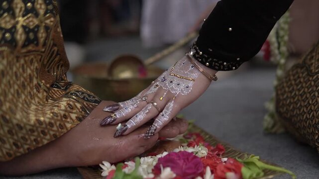 Javanese bride with white henna touching groom's feet during a traditional wedding ritual, 4K.