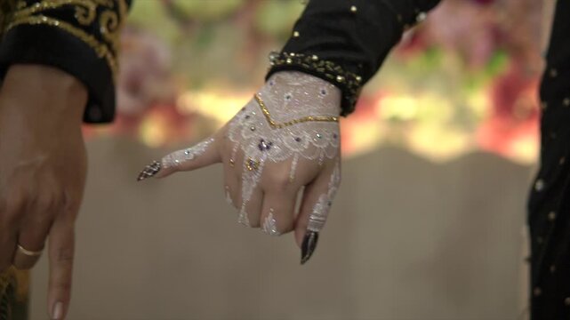 Close-up of a Javanese bride and groom's hands with white henna, interlocking pinky fingers, 4K.