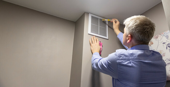 A person cleaning with a brush an HVAC return air vent grille and duct. Maintenance