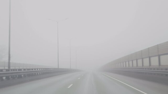 Heavy mist obscures busy road. Opaque fog surrounds multilane road with faint lights and damp surface creating suspenseful atmosphere