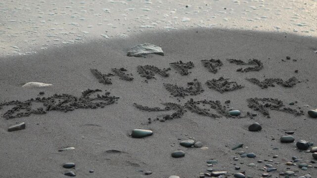 Sand writing new year. "Happy New Year 2026" message written on dark beach sand washed by calm ocean waves.