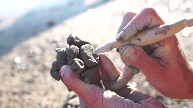 Clay sculpting hands meticulously create small artistic figure outdoors in bright sunlight, showcasing creativity and craftsmanship