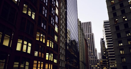 Obraz premium mirrored highrise reflecting neighboring brownstone and sky, narrow alley creating dramatic vertical perspective, evening office lights punctuating glass grid,