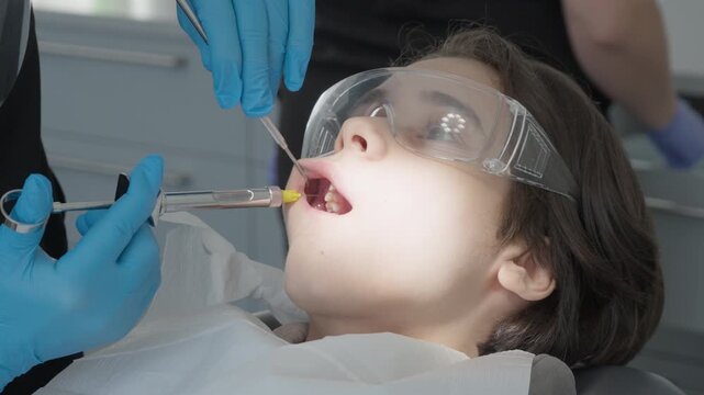 Pediatric dentist performing nerve block infiltration using carpal syringe. Administering pain relief medication to child patient before tooth extraction or cavity filling.