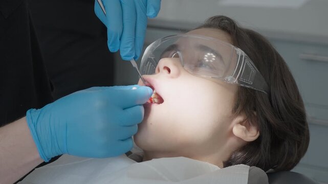 Doctor swabbing pediatric patient oral mucosa with local anesthetic gel before injection. Preparing boy for painless dental treatment in professional stomatology cabinet.