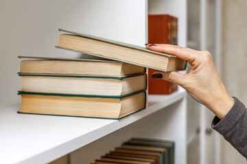 A woman's hand takes a book from a stack of books. hand takes a book, close-up. woman in the library