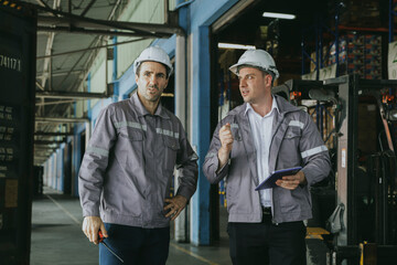 Two white male workers wearing safety vests and hard hats colleagues talking inspecting the loading yard container receiving goods storage area industrial warehouse unloading logistics transportation.