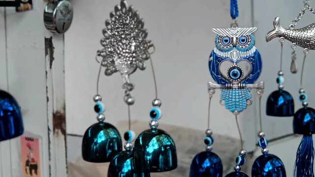 A decorative hanging ornament, a wind chime, featuring an intricate silver-toned metallic peacock top. Dark, reflective blue bell-shaped elements hang below, with small silver & blue beads.