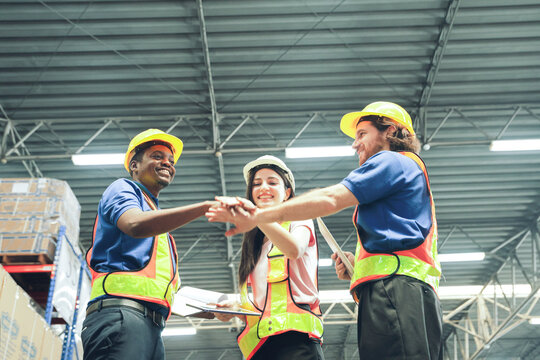 Workers working together : Working team in a lare industrial warehouse diverse group of men and women all wearing safety vests and hard hats join hands and combine their strength for cooperation and s