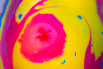 Macro abstract composition of bright yellow liquid paint flowing through bright pink with subtle blue edges and small white droplets, creating smooth fluid curves and dynamic color contrast.