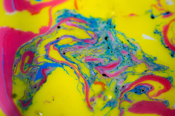 Macro image of swirling neon paint in bright yellow, pink and blue forming flowing marble-like patterns and organic shapes. Highly saturated abstract texture with dynamic movement and artistic color f