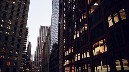 Obraz premium narrow urban canyon at dusk showing brownstone facades and warm office windows, empty street below, moody cinematic lighting, golden reflections on glass,