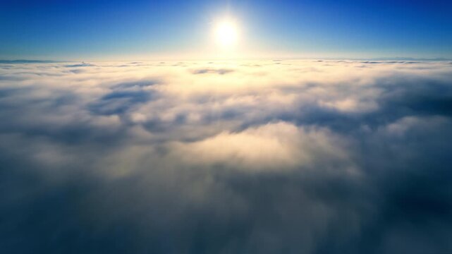Aerial time lapse of flowing fog in morning sunlight, with the sun in the clear blue sky