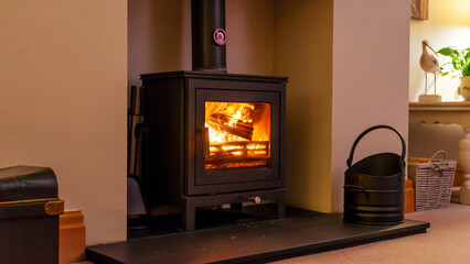 An iron fireplace with a chimney in a room with dim lighting. Fire in an iron stove in a living room in the evening © mikus